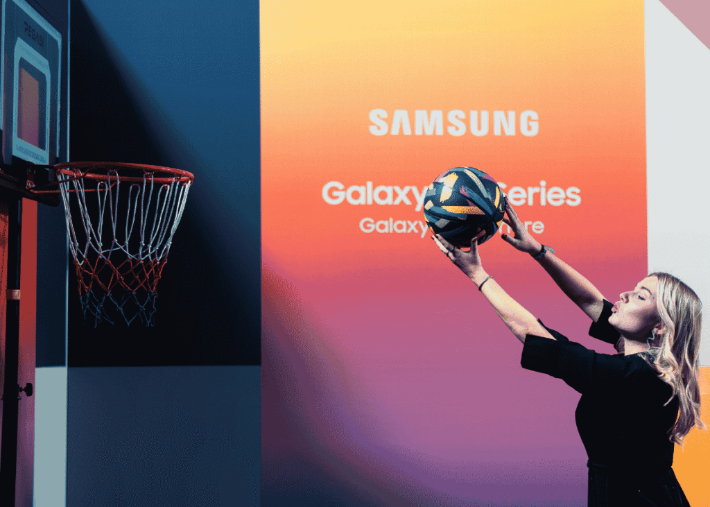 Gepersonaliseerd HOYA-figuurtje in speelgoedverpakking, met een oogtestkaart, bril en andere accessoires. Bezoeker schiet een basketbal tijdens een interactieve Samsung Galaxy Series-brand activation.